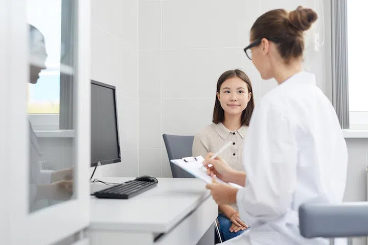 Portrait of little Asian girl listening to female doctor during consultation, copy space