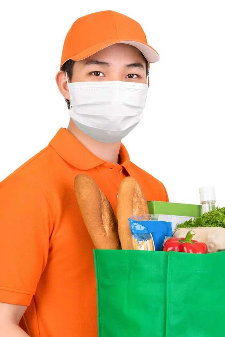 Hygienic man wearing medical mask carrying supermarket grocery shopping bag offering home delivery service isolated in white background