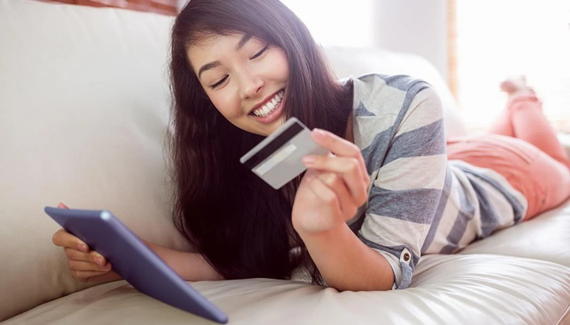 Smiling asian woman on couch using tablet to shop online at home in the living room