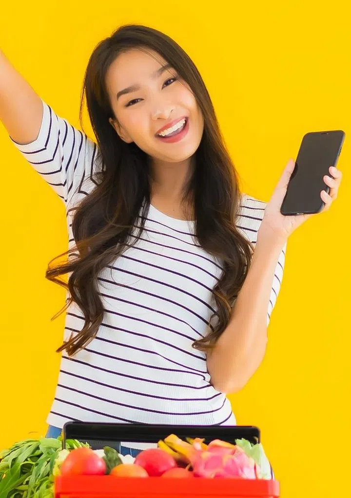 Portrait beautiful young asian woman shopping grocery from supermarket and cart with smart mobile phone on yellow isolated background