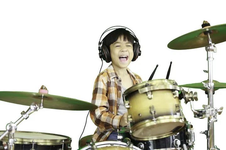 A cute Asian boy is enjoying playing the drums in a music classroom. An isolated image with white background.