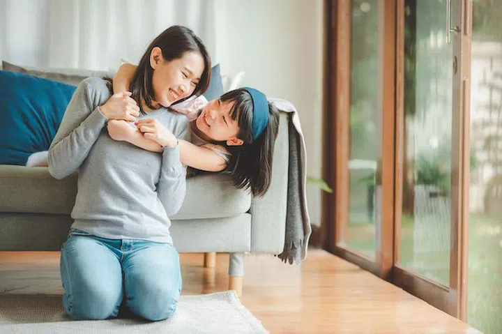 Happy Asian mother and cute little daughter having fun while playing and hugging at home in living room