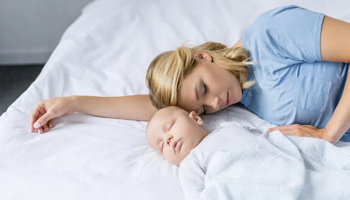 portrait of mother and infant baby sleeping on bed together