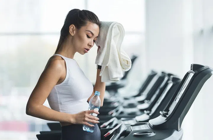 Woman tired and having rest after running on treadmill in modern gym