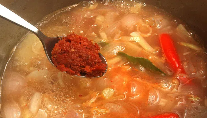 03. Add the red chilli and green chilli. Add eight kaffir lime leaves and the chilli padi. Add the dried chilli paste and stir.