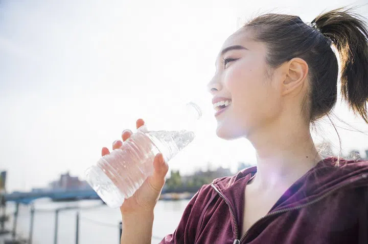 Japanese young woman drinking cold water at riverside park