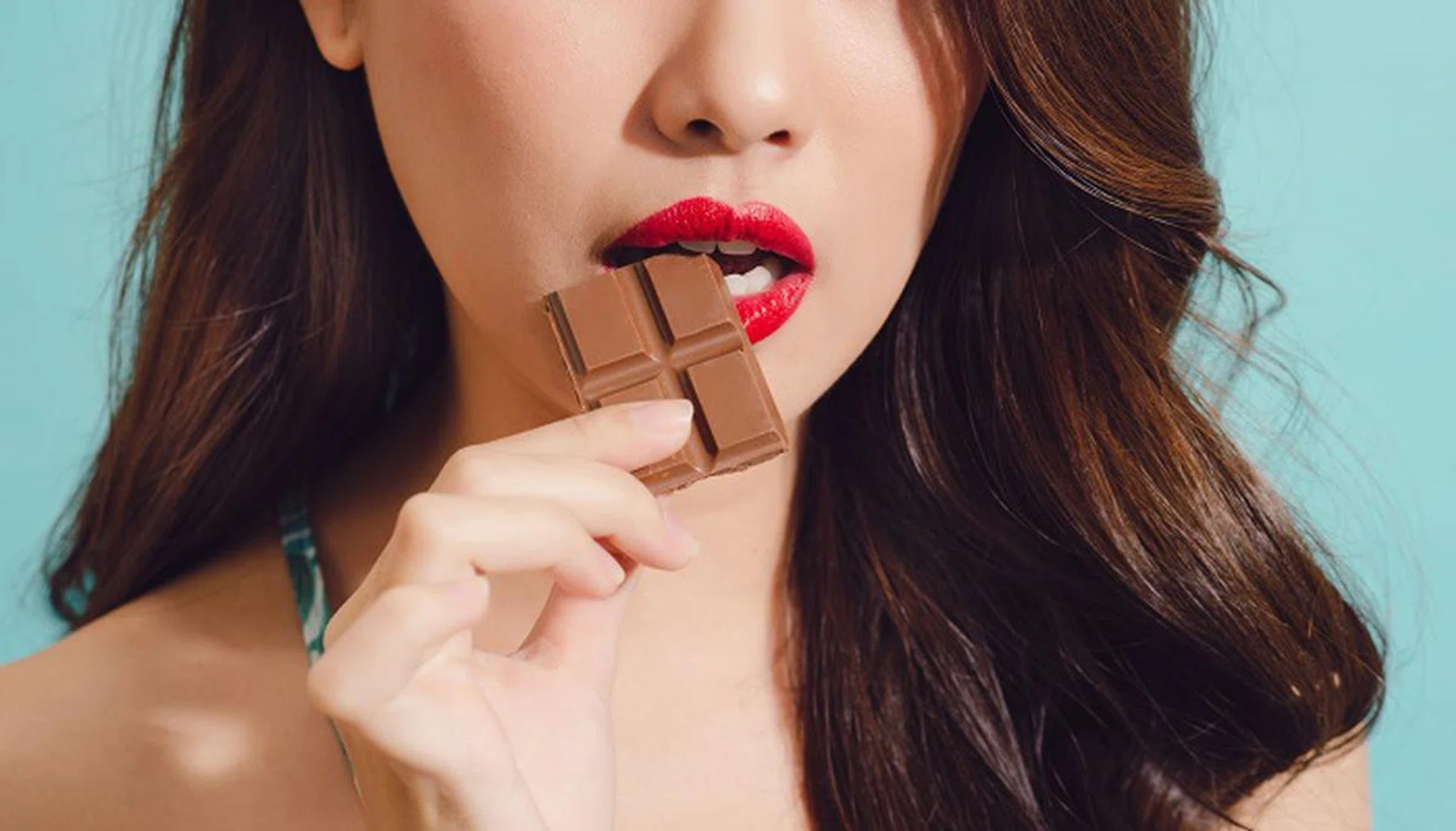 Attractive young asian woman eating chocolate, closeup