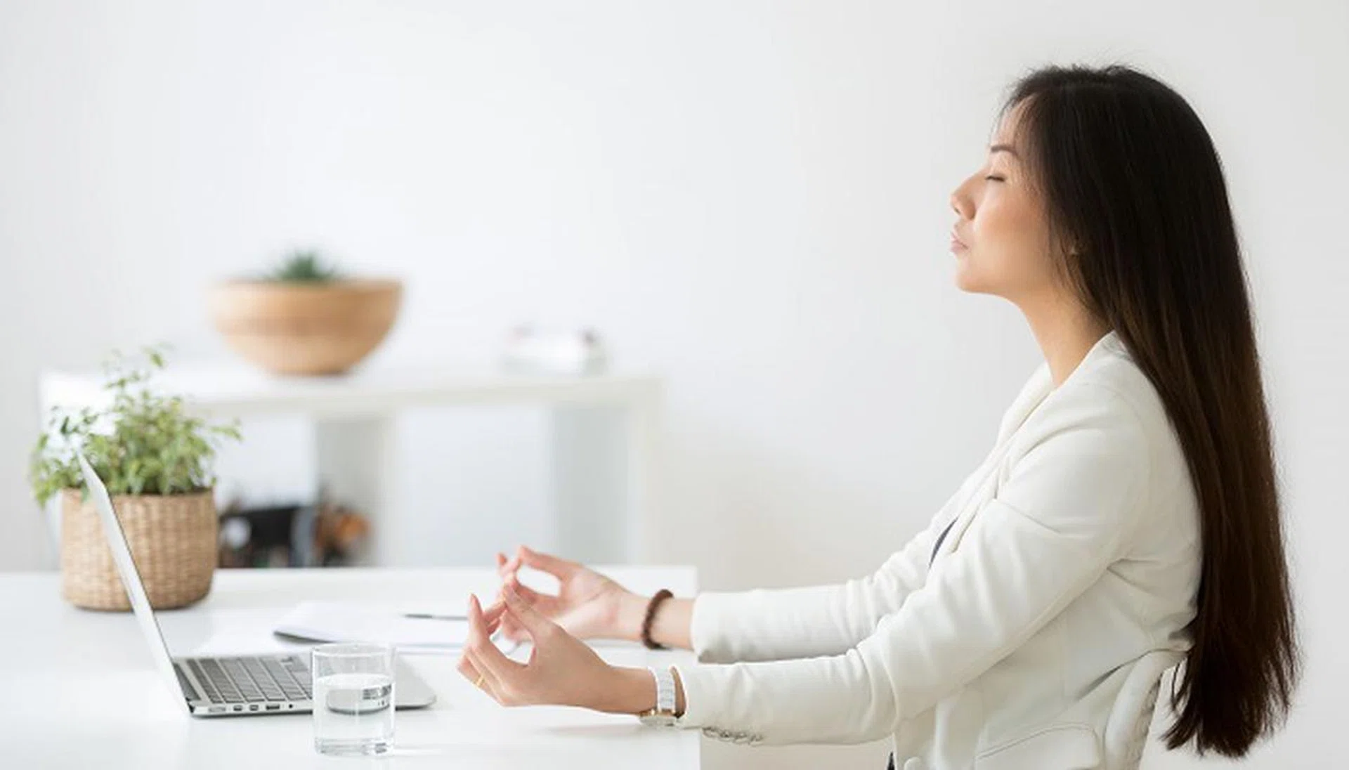 Calm thoughtful Asian female employee sitting at office desk meditating, practicing yoga, controlling emotions, young businesswoman searching for balance, relieving stress at work. Mindfulness concept