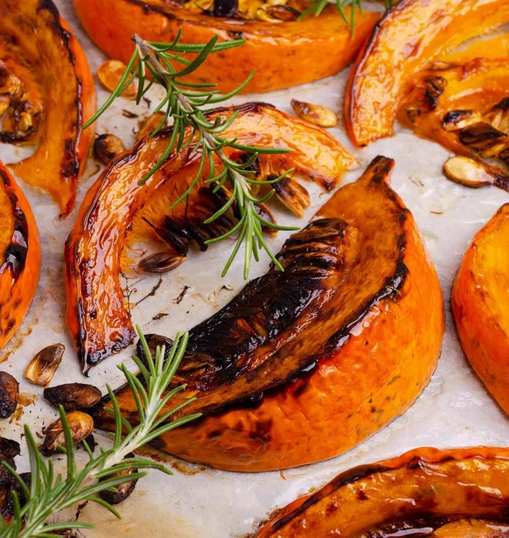 Baked pumpkin slices with seeds and rosemary on paper. Selective focus.