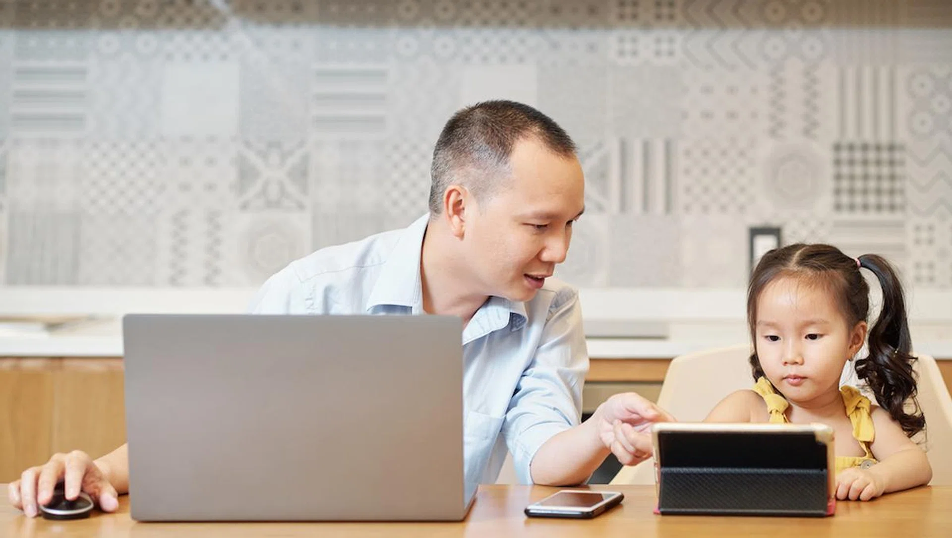 Father helping daughter to find cartoon to watch online on tablet computer when they are sitting at kitchn table