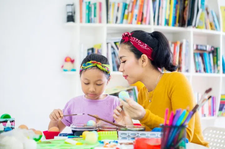 Young woman and her daughter coloring eggs for Easter in the library