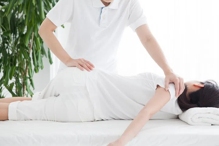 A woman lying on the bed and receiving rehabilitation.