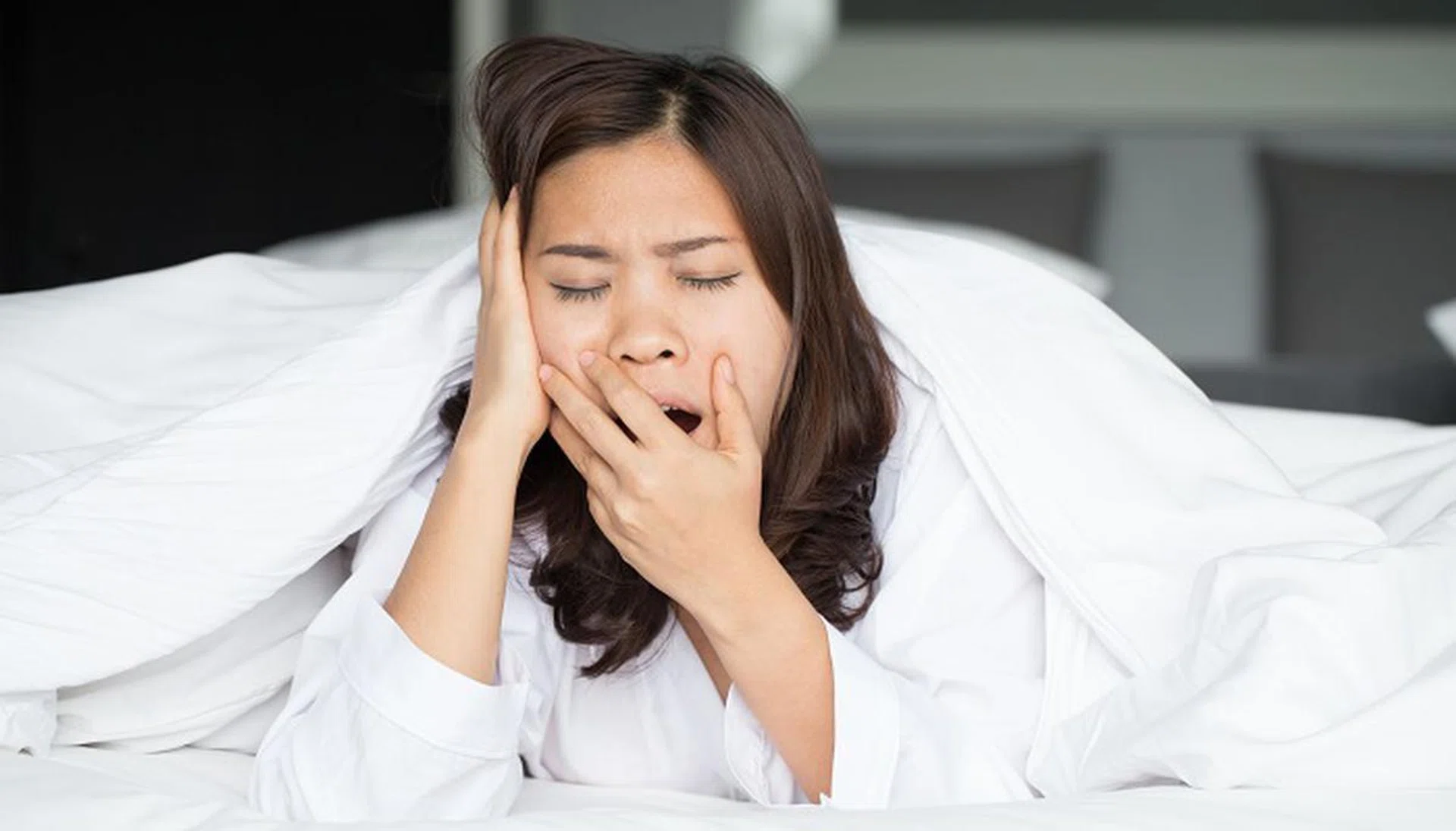 Sleepy asian woman yawning in bed at home