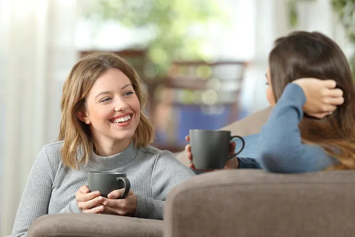 Two happy friends having a casual conversation sitting on a couch in the living room at home