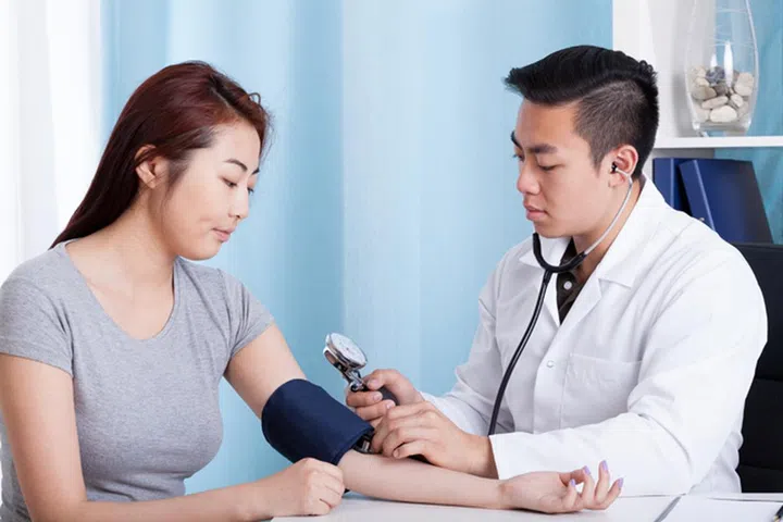 Asian male doctor taking blood pressure of a female patient