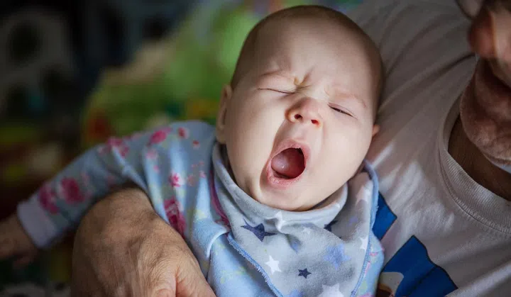 Baby girl yawning. Cropped view of grandfather rocking baby to sleep.