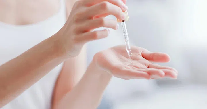beautiful woman dropping collagen moisturizer into her hand at home