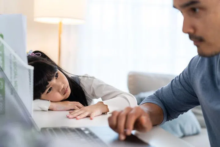 Asian young kid daughter feeling sad and need to play with busy father. Attractive parent daddy use laptop computer working from home during new normal and have no time for little child girl in house.