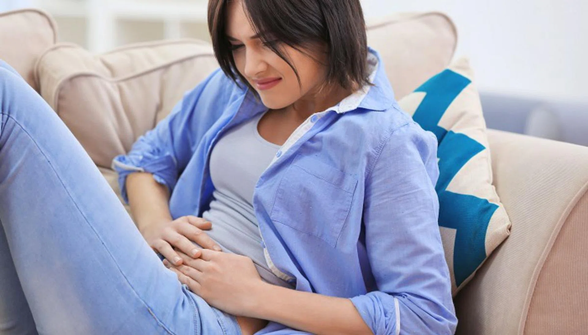 Beautiful young woman suffering from abdominal pain while sitting on sofa at home