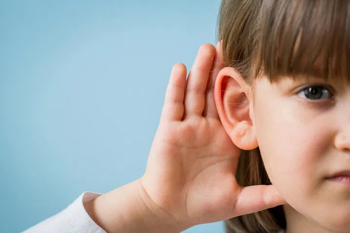 Child with hearing problem on blue background. Hearing loss in childhood, symptoms and treatment concept. Close up, copy space.