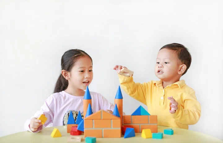 Asian little child girl and baby boy playing a colorful wood block toy on table over white background. Sister and her brother playing together.