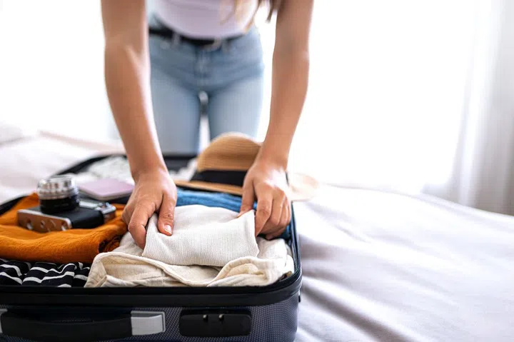 Unrecognizable young woman packing suitcase for summer vacation trip. Copy space. Holiday, tourist, vacation concept.