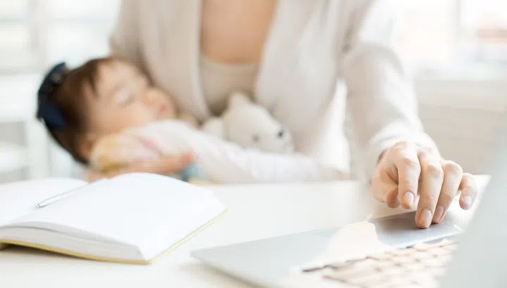 Hand of business mother on laptop keypad during network in office with sleeping baby in the other one