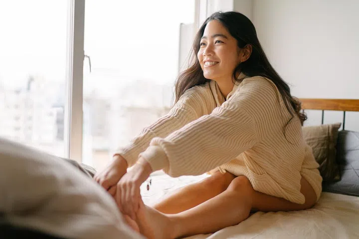 A young woman is stretching her legs for the rest of the day on her bed.
