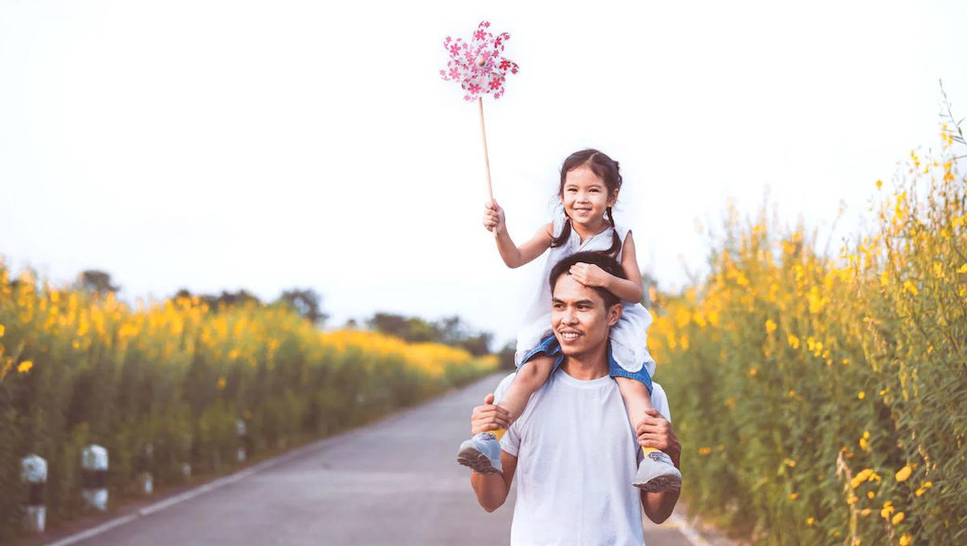 Cute asian little girl playing with wind turbine and riding on father's shoulders in the flower garden in vintage color tone. Father and daughter having fun to play together.