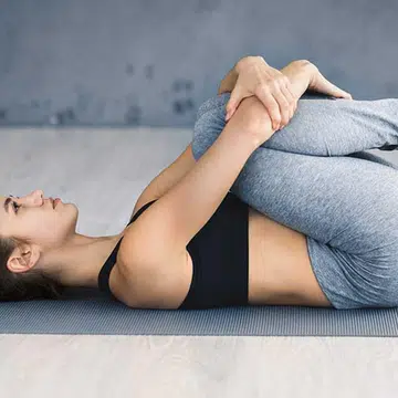We're almost there – just two more yoga poses to go to help you improve your digestion. Now, continue to lie on your back. Bring your knees into your chest, and hug your knees with your arms.