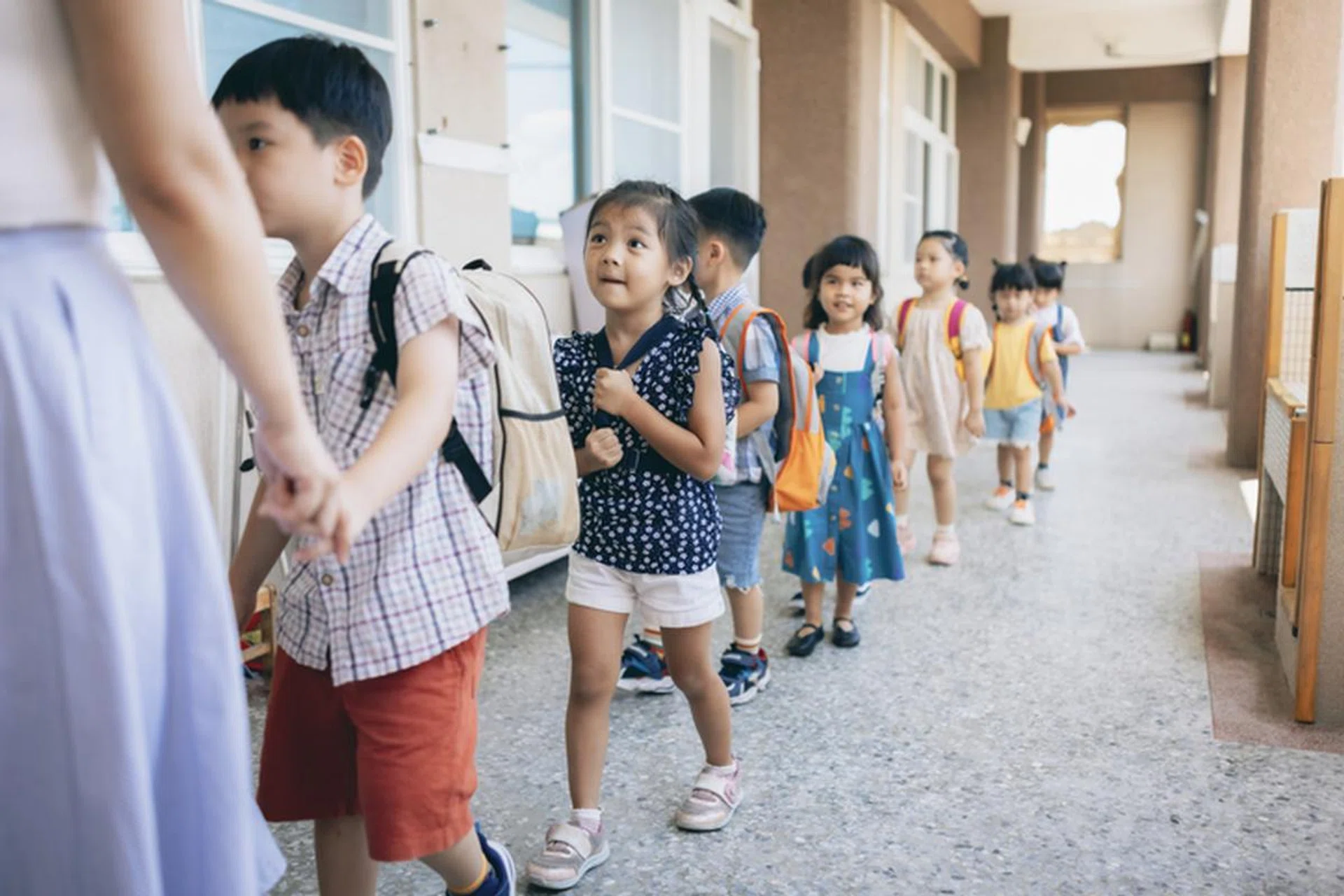 Preschool teacher guiding and arranging students waiting in line entering classroom
