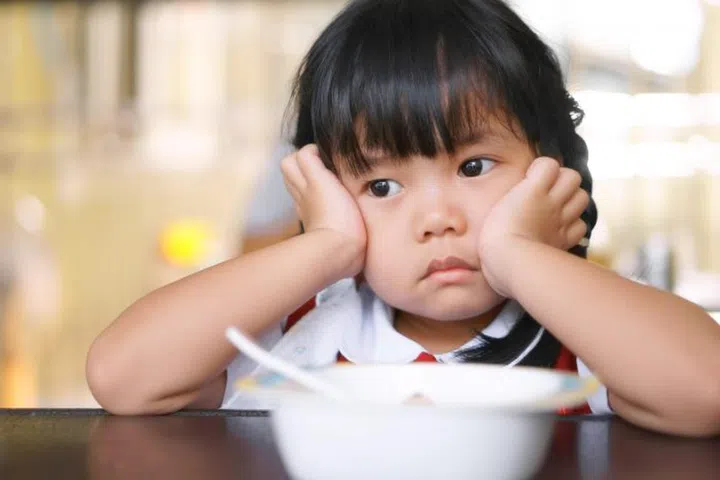 Asian children cute or kid girl student anorexia or sad with vacant and prop up or hand to cheek on food table for breakfast before going to school for study
