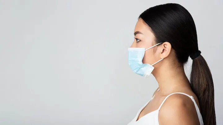Infection concept. Asian girl wearing medical mask and looking at free space, grey background, side view