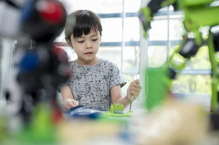 Asian preschool girls wearing hearing aids while learning on a robot assembly in classroom. Improve Kids learning skill and motivative concetps.