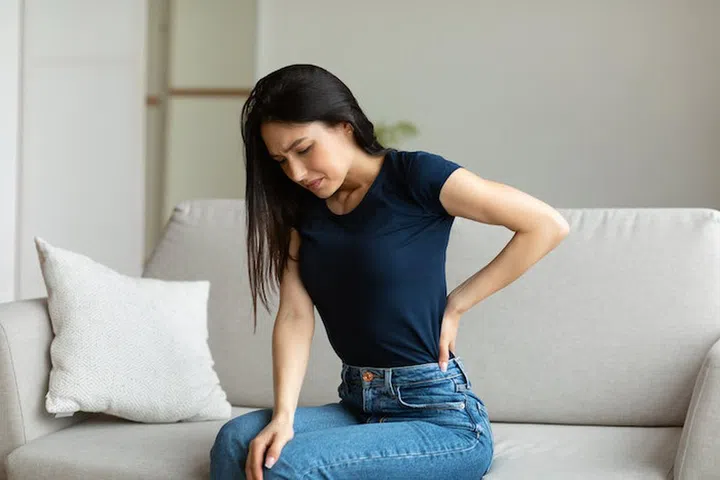 Back Pain. Woman Suffering From Backache Having Spine Problems Sitting On Couch At Home.