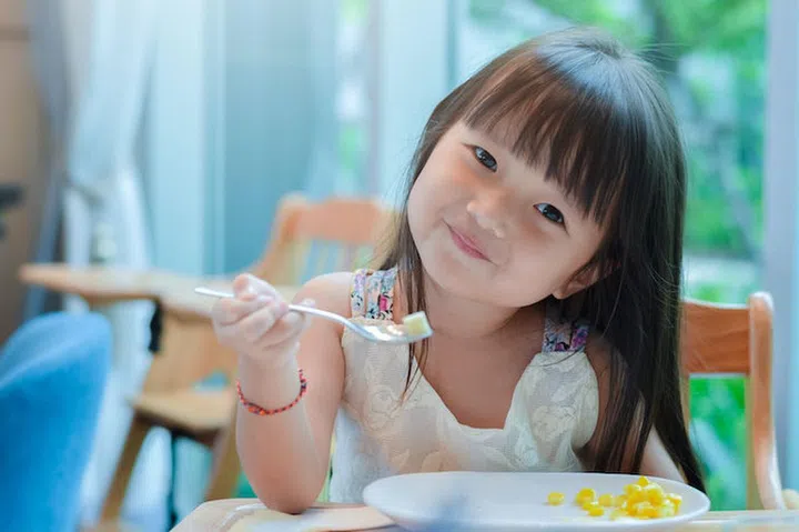 Little asian child girl having breakfast at the morning with a happy smiling face and showing food on a spoon