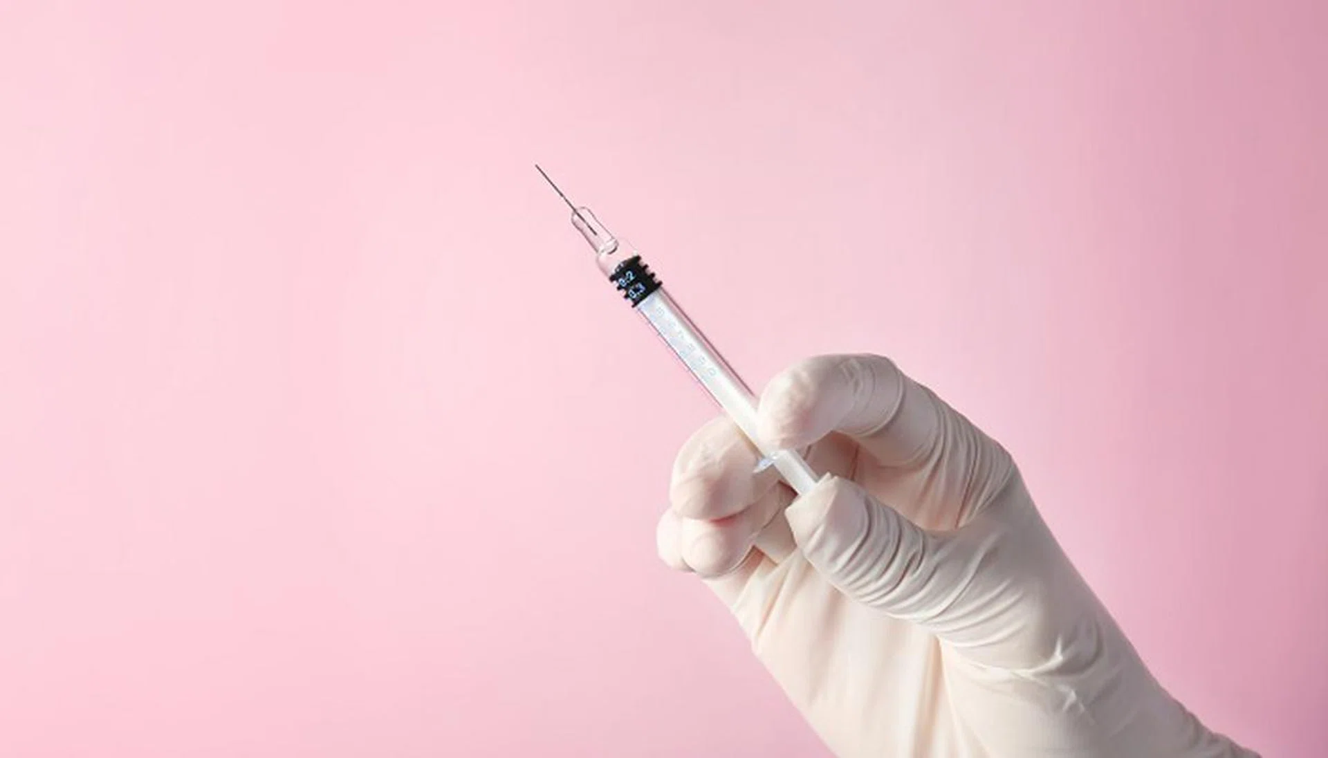 Hand of nurse with syringe prepared for vaccination, on pink background