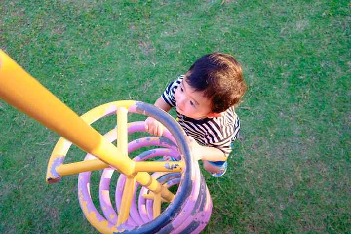 Active little child playing climbing spring metal at school yard playground. Kids play and climb outdoors under sunset,  shallow Focus.