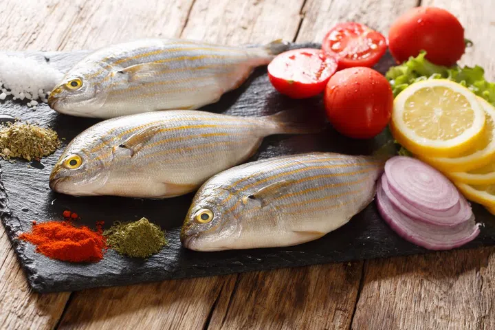 Freshly caught Sarpa salpa with raw vegetables and spices close-up on a slate board on the table. horizontal