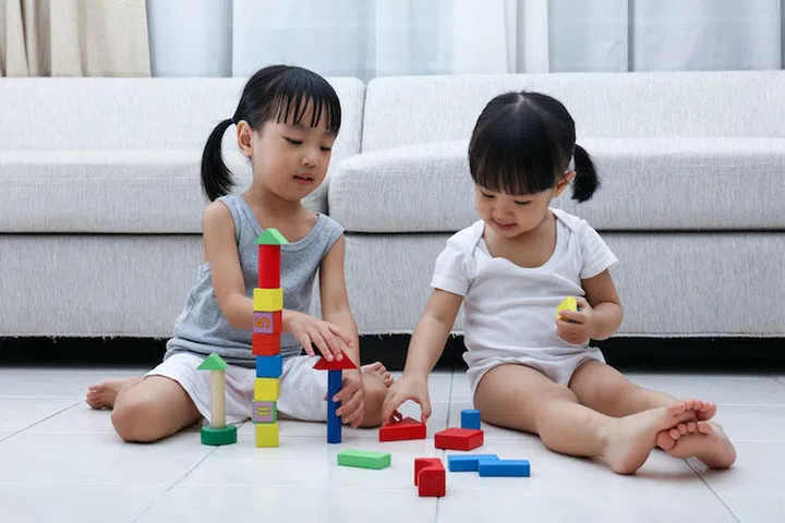 Asian Chinese little sisters playing blocks on the floor in the living room at home.