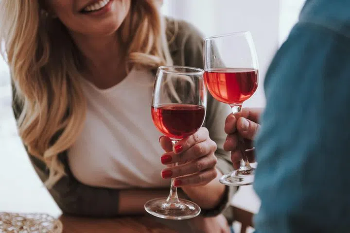 Close up of wife and husband clinking glasses of alcoholic drinks. Charming lady leaning on table and smiling