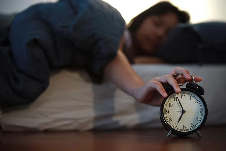 Upon waking up early in the morning, a young Asian girl tried to turn off the alarm clock in her bedroom at home while still lying in bed