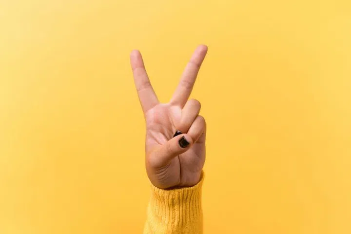 Hand gesture V sign for victory or peace sign over yellow background