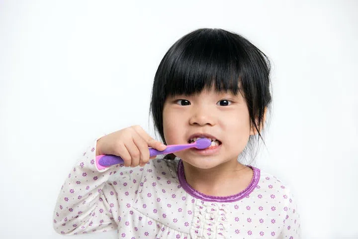 Little Asian girl in pyjamas brushing teeth