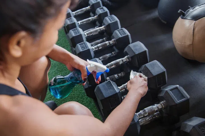 Portrait shot of female athlete cleaning dumbbells before workout ,precautions of Coronavirus