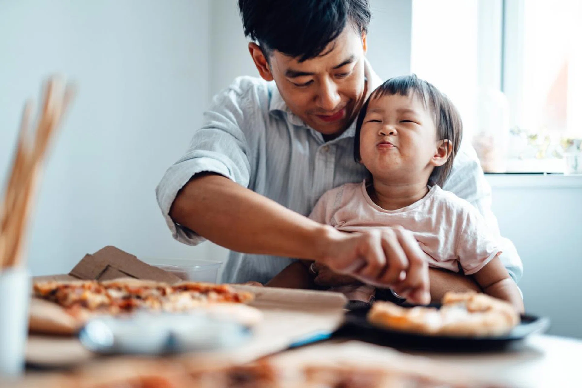 Young Asian dad feeding food for his baby daughter at home. Caring and togetherness concept.
