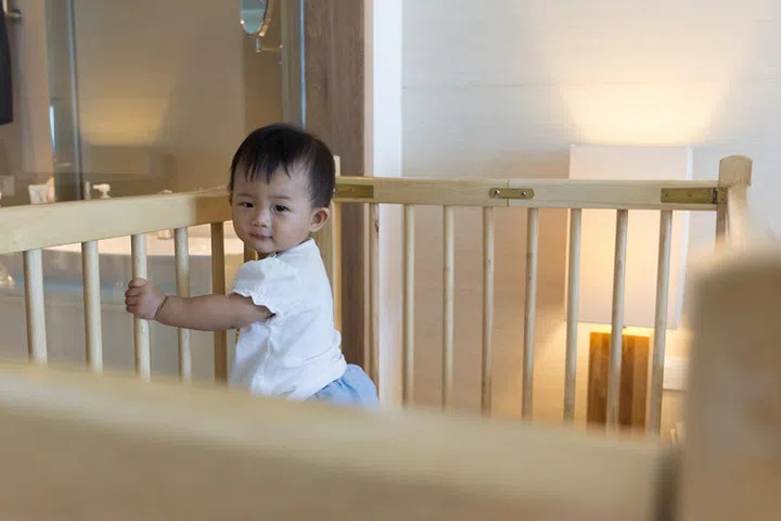 Asian cute baby standing on baby cot in luxury bed room hotel.