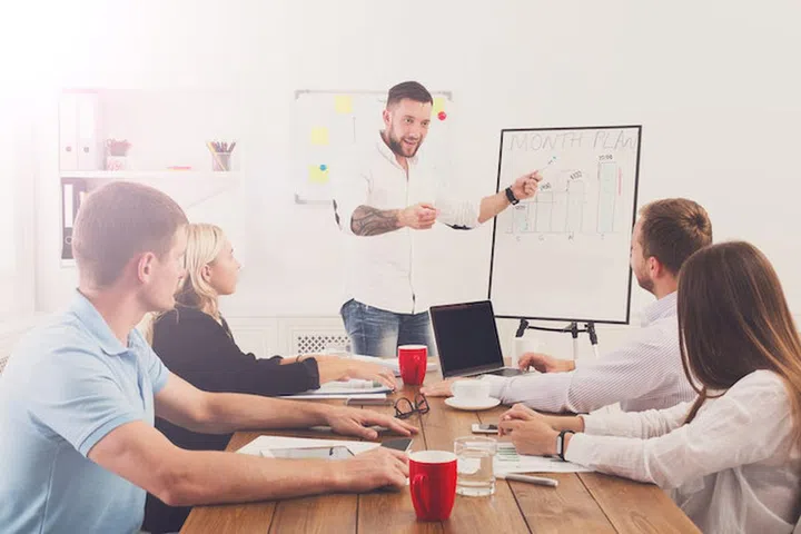 Project presentation. Young happy businessmen and women at modern office, team corporate discussion at workplace, show information on board. Brainstorming and communication with partners for startup