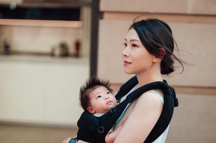 Beautiful Asian mum holding her baby in baby carrier while walking in the city. Love and protection. Motherhood. Mother bonding with her baby.