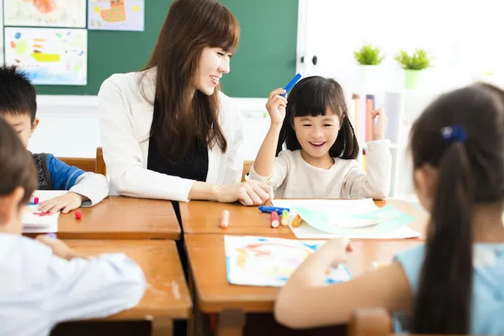 happy children drawing in the classroom and teacher near by
